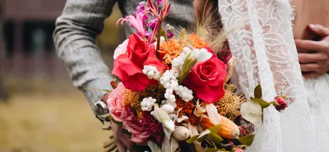 Barevná svatební kytice s červenými růžemi v rukou nevěsty.